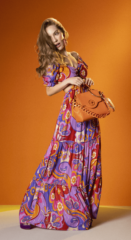 Mujer usando vestido largo estampado de la marca Studio F y un bolso de manos color café