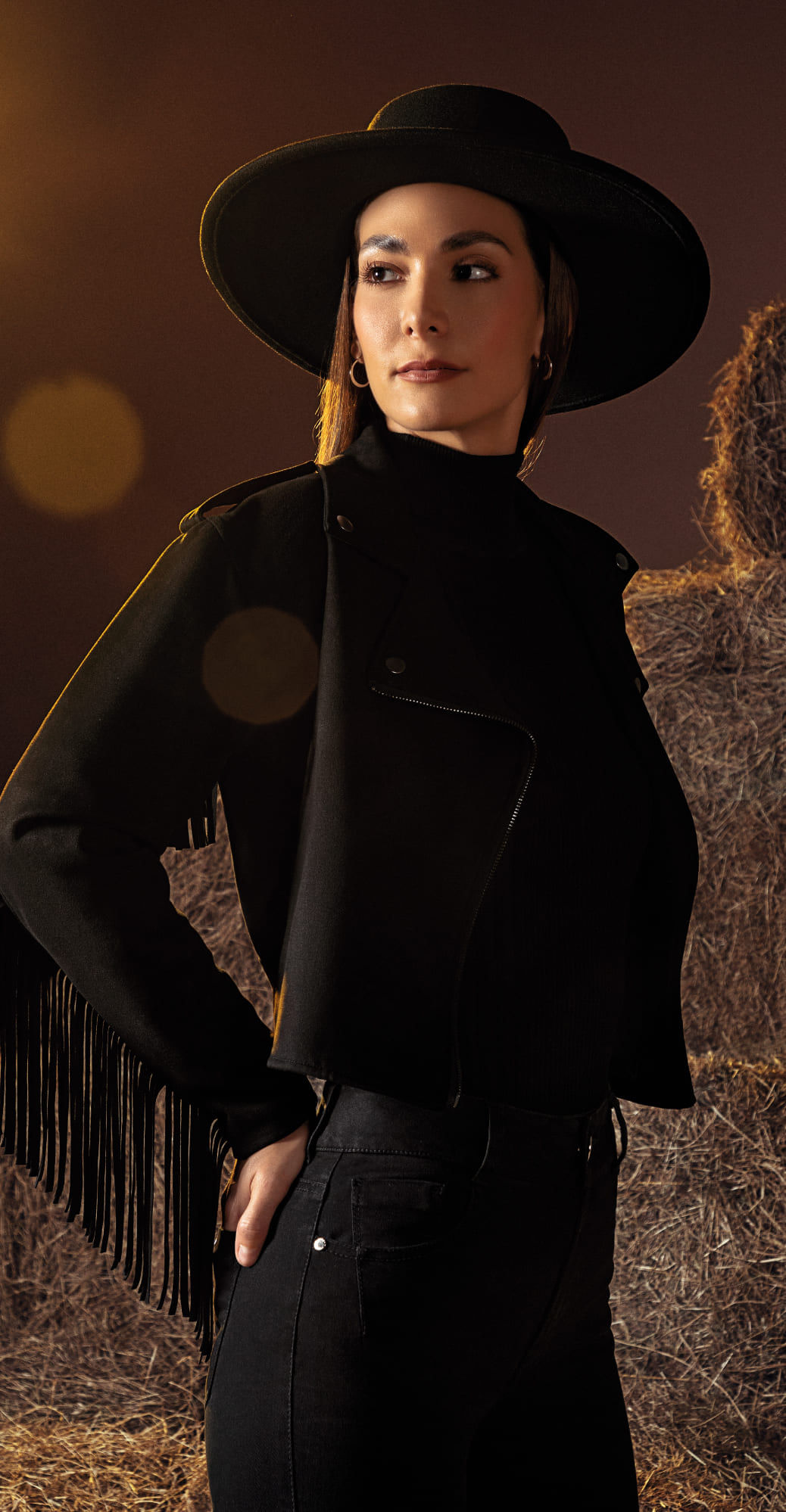 Fotografía de mujer posando con chamarra de manga con flecos café, jean slim y sombrero como complemento