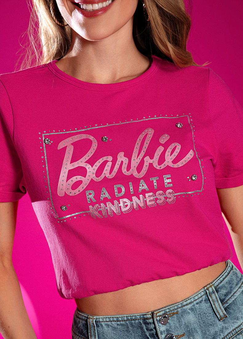 Foto en plano medio de mujer usando camiseta de Barbie color rosa con estampado metalizado plateado.