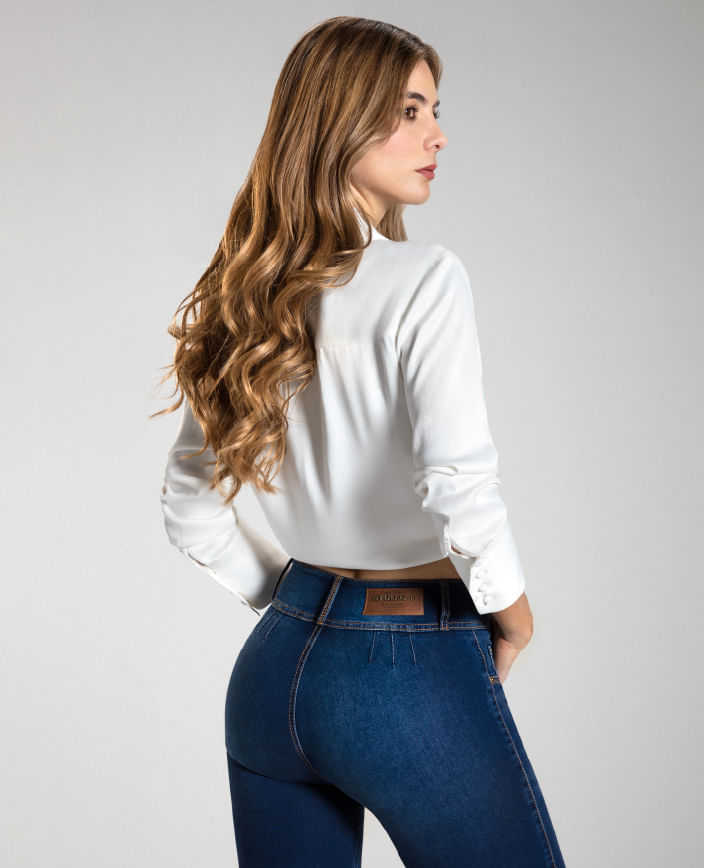 Foto en plano americano de mujer dando la espalda vistiendo jean sin bolsillos pretina ancha y camisa manga larga blanca