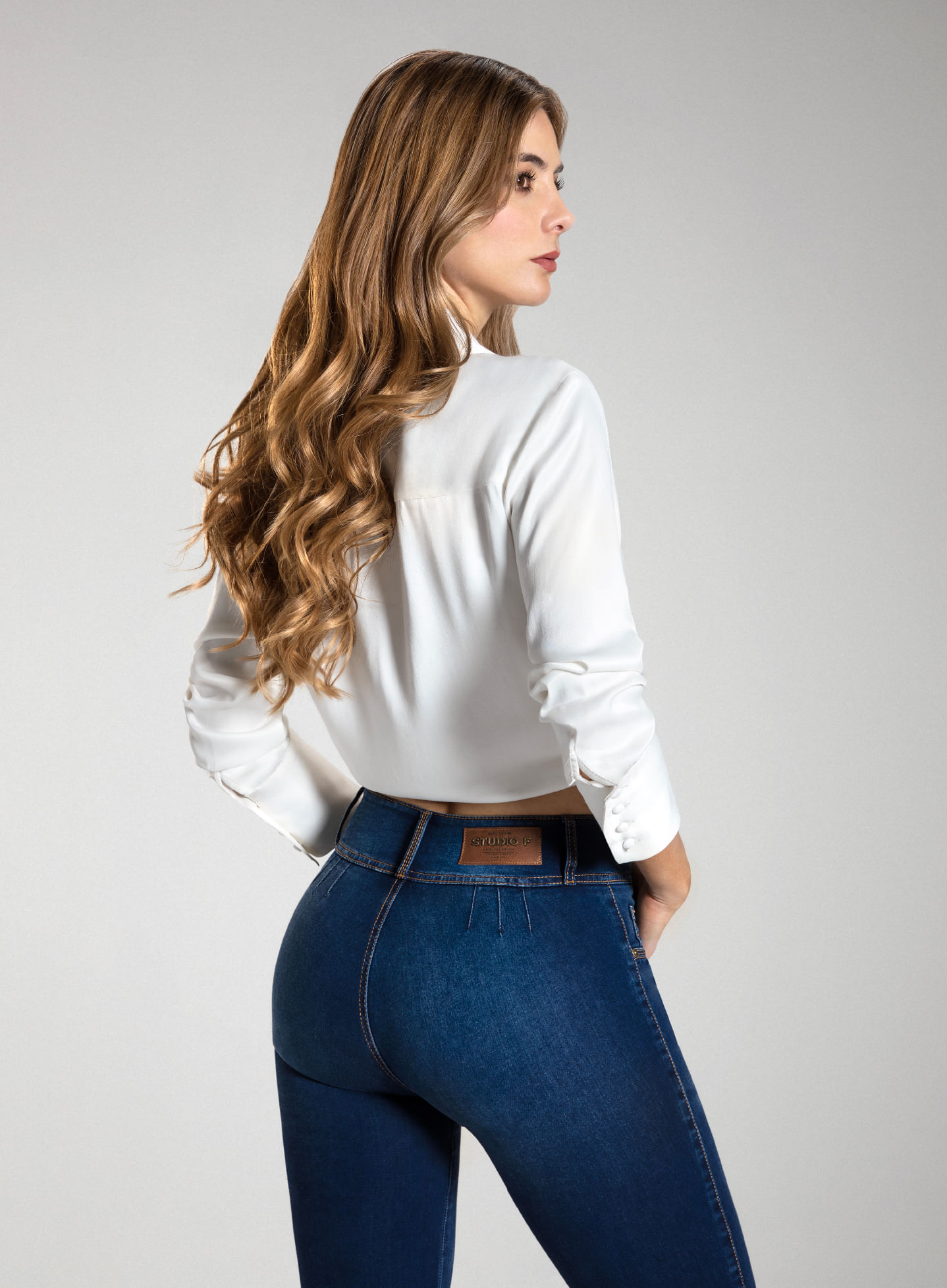 Foto en plano americano de mujer dando la espalda vistiendo jean sin bolsillos pretina ancha y camisa manga larga blanca