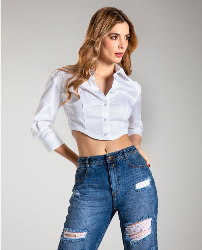 Foto en plano americano de mujer usando blusa crop blanca con manga larga y jean boyfriend con rotos