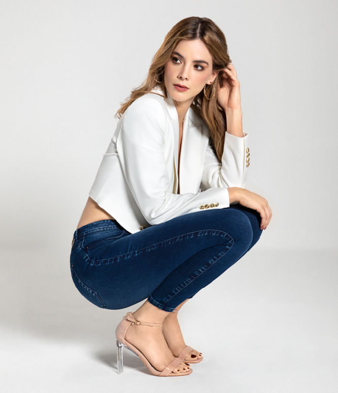 Mujer de cuclillas usando jean 5 bolsillos, tiro alto, blazer blanco y tacones Studio F