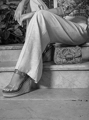 Foto en blanco y negro primer plano de mujer sentada usando sandalias de plataforma y pantalón