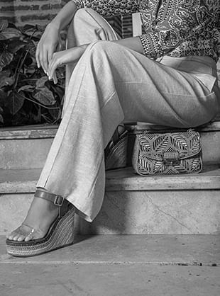 Foto en blanco y negro primer plano de mujer sentada usando sandalias de plataforma y pantalón