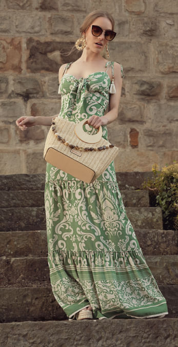 Modelo usando vestido largo verde estampado, bolso de mano, gafas de sol y aretes redondos de la última colección Damasco premium
