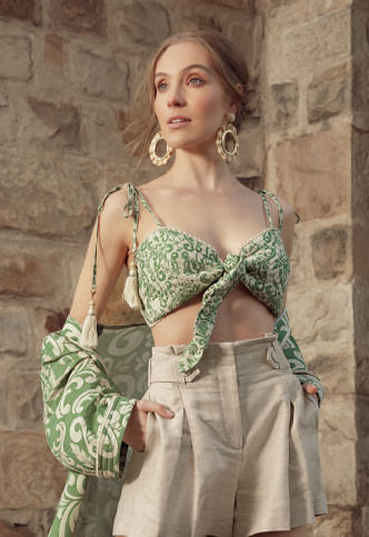 Mujer usando crop top de tiras verde estampado, pantalón beige y aretes redondos grandes de la marca Studio F
