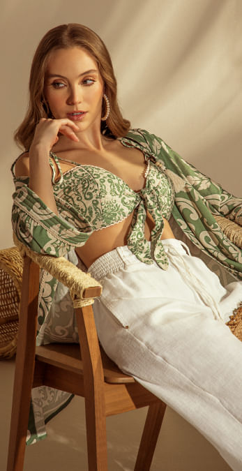 Foto en plano americano de mujer usando crop top de tiras, pantalón blanco y sobretodo verde estampado. 