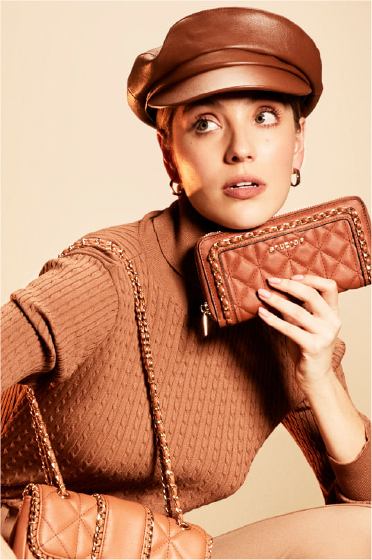 Mujer posando y vistiendo blusa cuello tortuga, pantalón, bolso, billetera y boina en tonos café