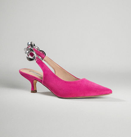 Zapato cerrado de tacón en color rosa con aplique decorativo plateado en la parte trasera.